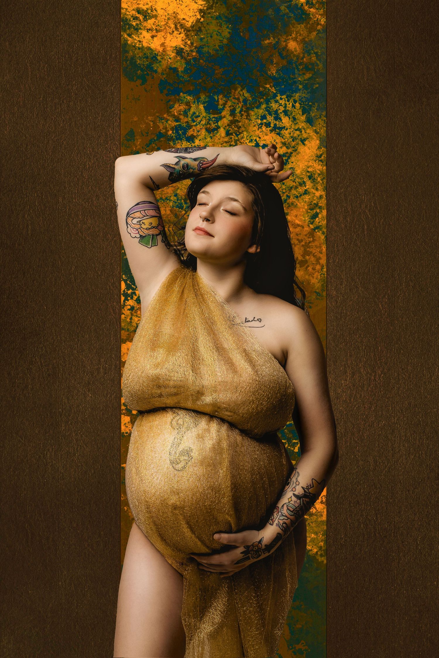 Artistic maternity portrait in gold fabric against orange and teal backdrop.