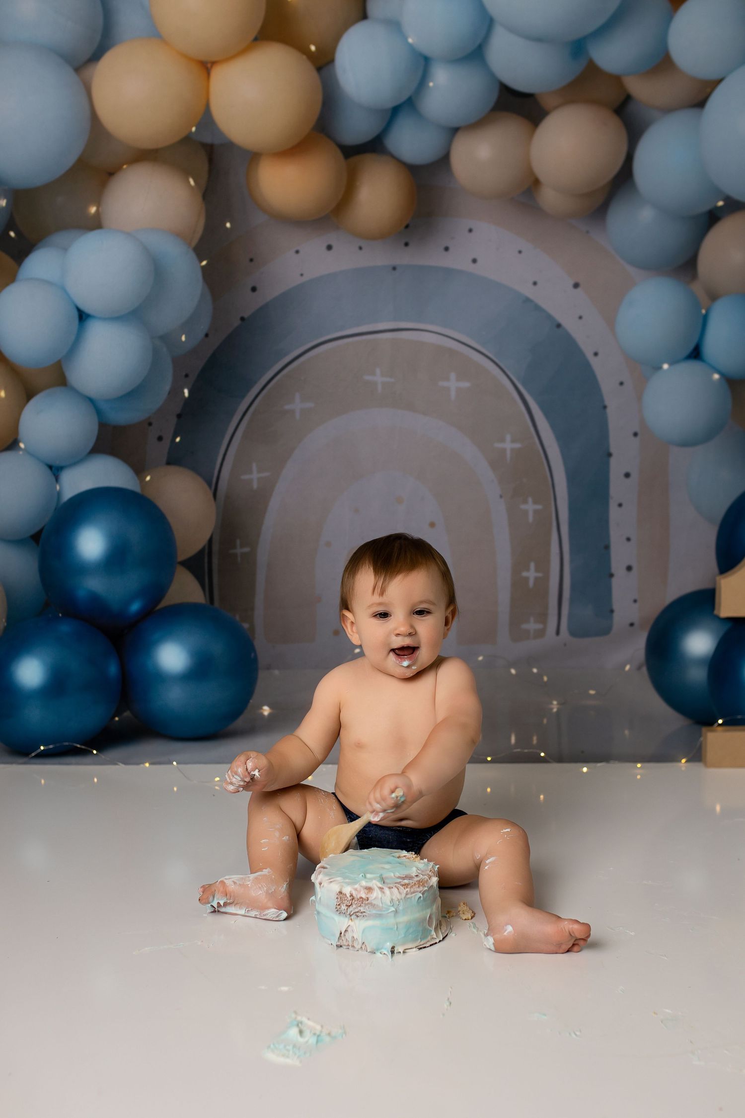 Baby's first birthday cake smash with blue and tan balloon arch backdrop.