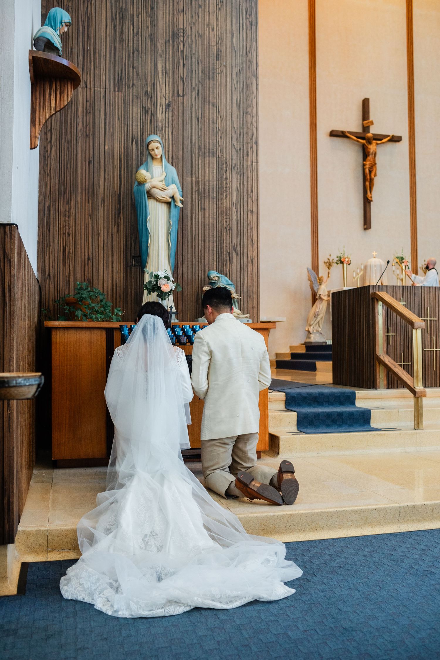 Wedding ceremony taking place in modern church sanctuary with wooden panels and religious statues.