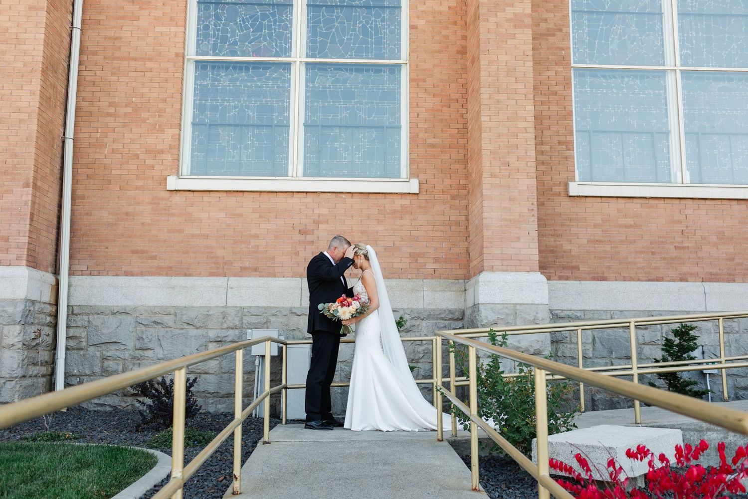 Couple poses for wedding photos on brick steps with railing outside church entrance.