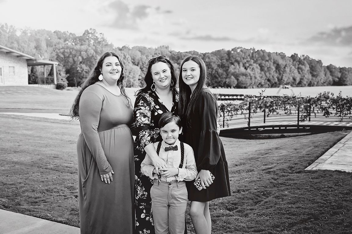 Group portrait in black and white taken outdoors with vineyard in background.