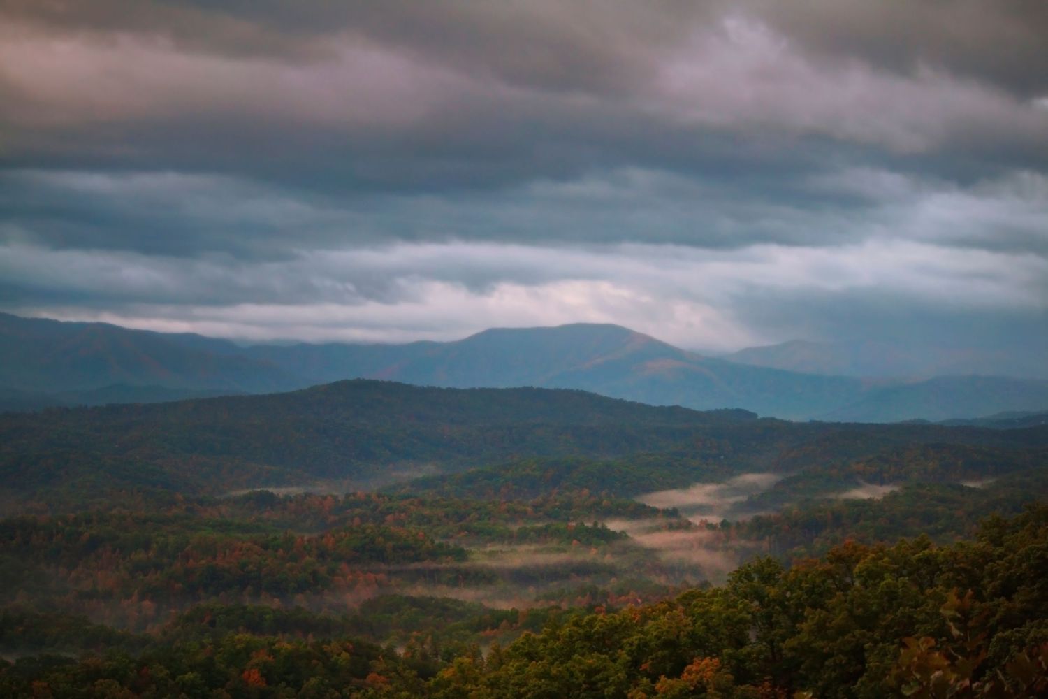 Misty mountain landscape with rolling hills under dramatic stormy clouds.