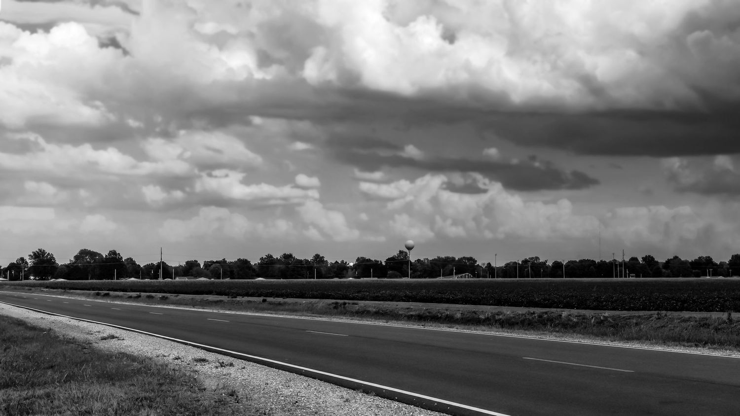 Black and white photograph of a curved highway under dramatic cloudy skies.
