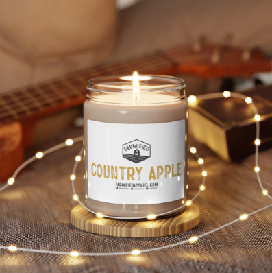 Lit Country Apple scented candle in a glass jar on gold coaster with string lights in the background.