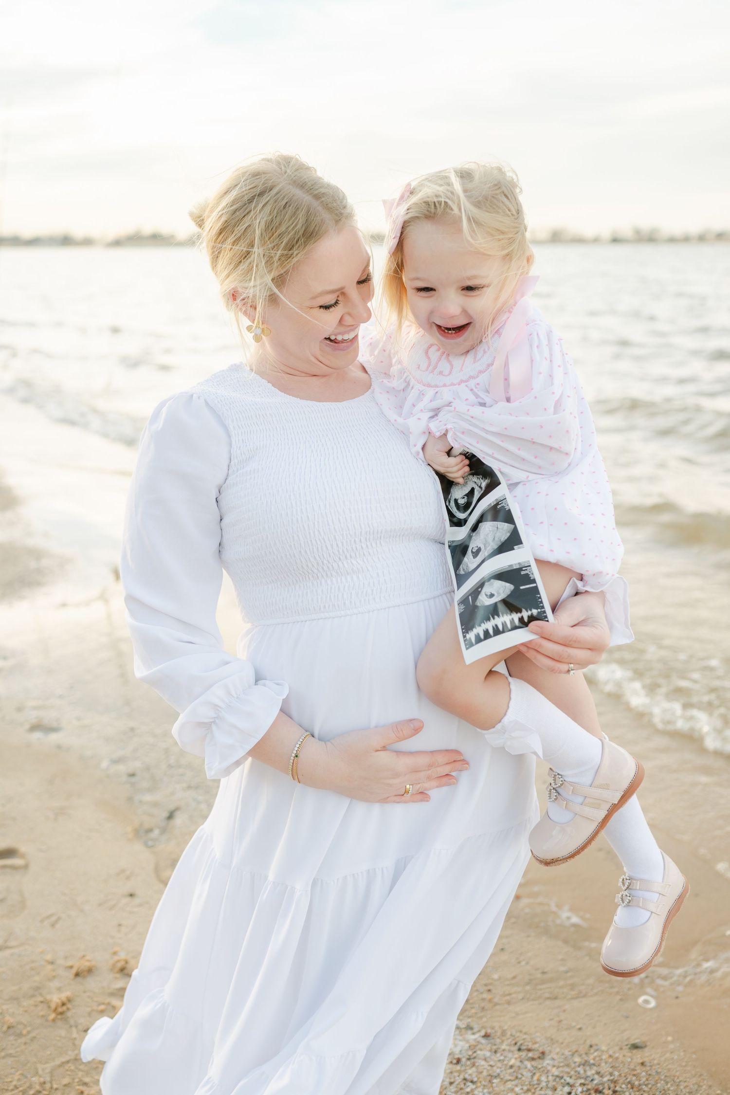 Mother holding belly with child in arms in front of Lake Hefner in Oklahoma City, OK for Family photographer
