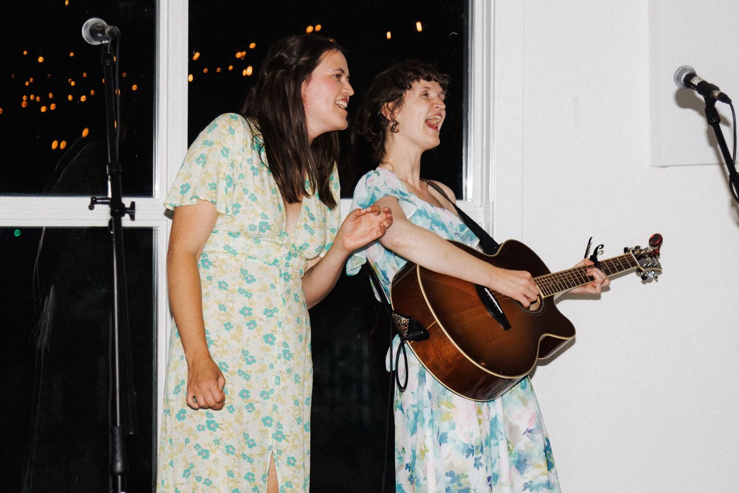 Musicians perform in floral dresses at wedding, one singing, one on guitar, captured by Kaitlyn Yvette in Newfoundland.