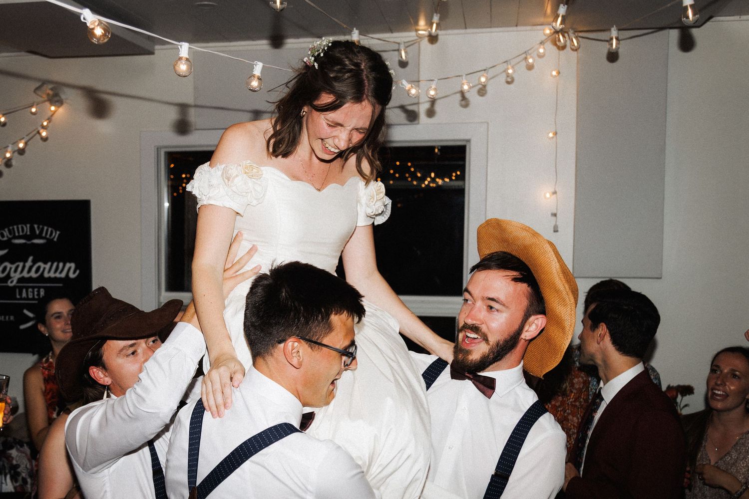 Guests lift bride during dance party under string lights at Quidi Vidi, by Kaitlyn Yvette, Newfoundland wedding photographer.