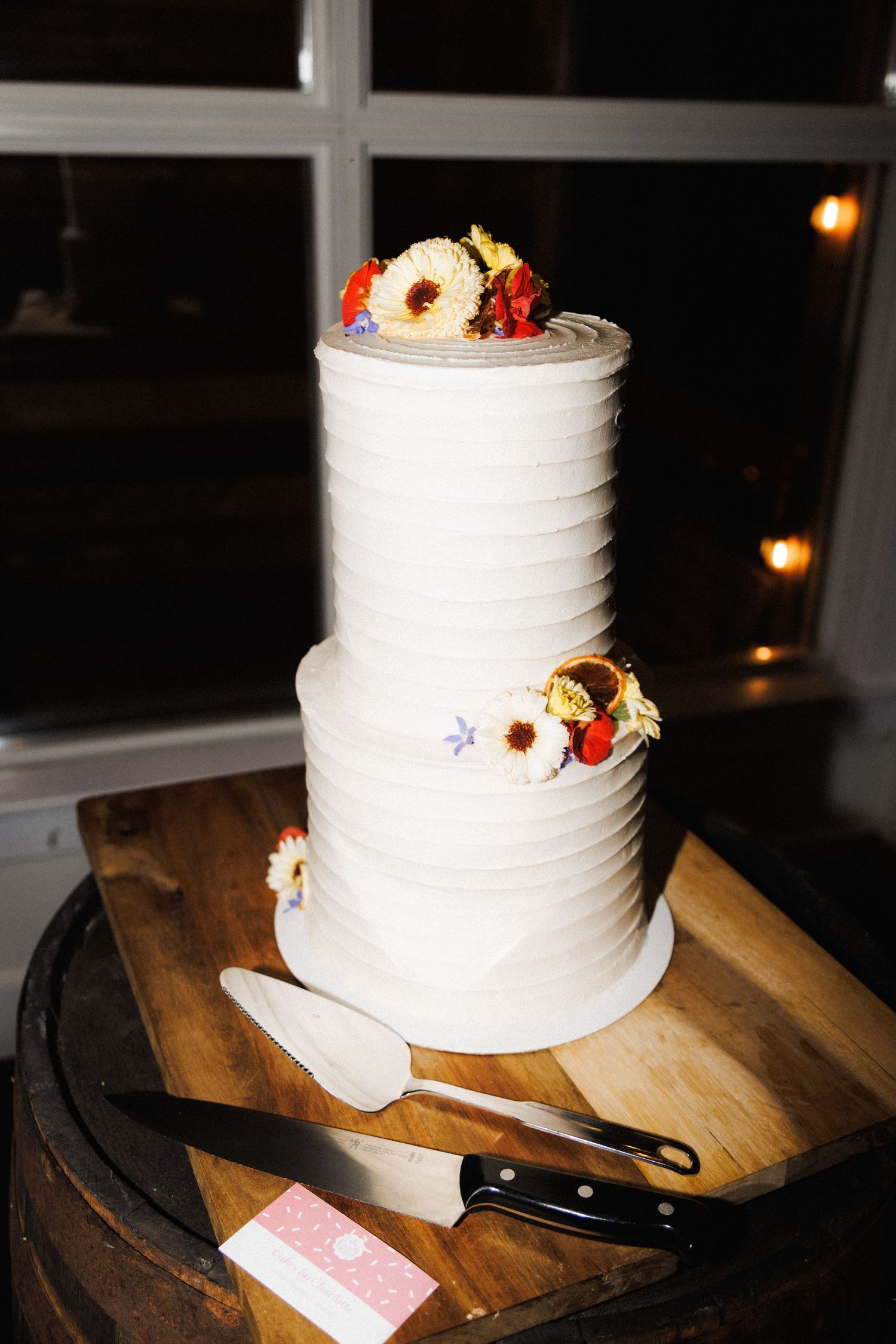 White two-tiered wedding cake with florals on wood board, photographed by Newfoundland wedding photographer Kaitlyn Yvette.