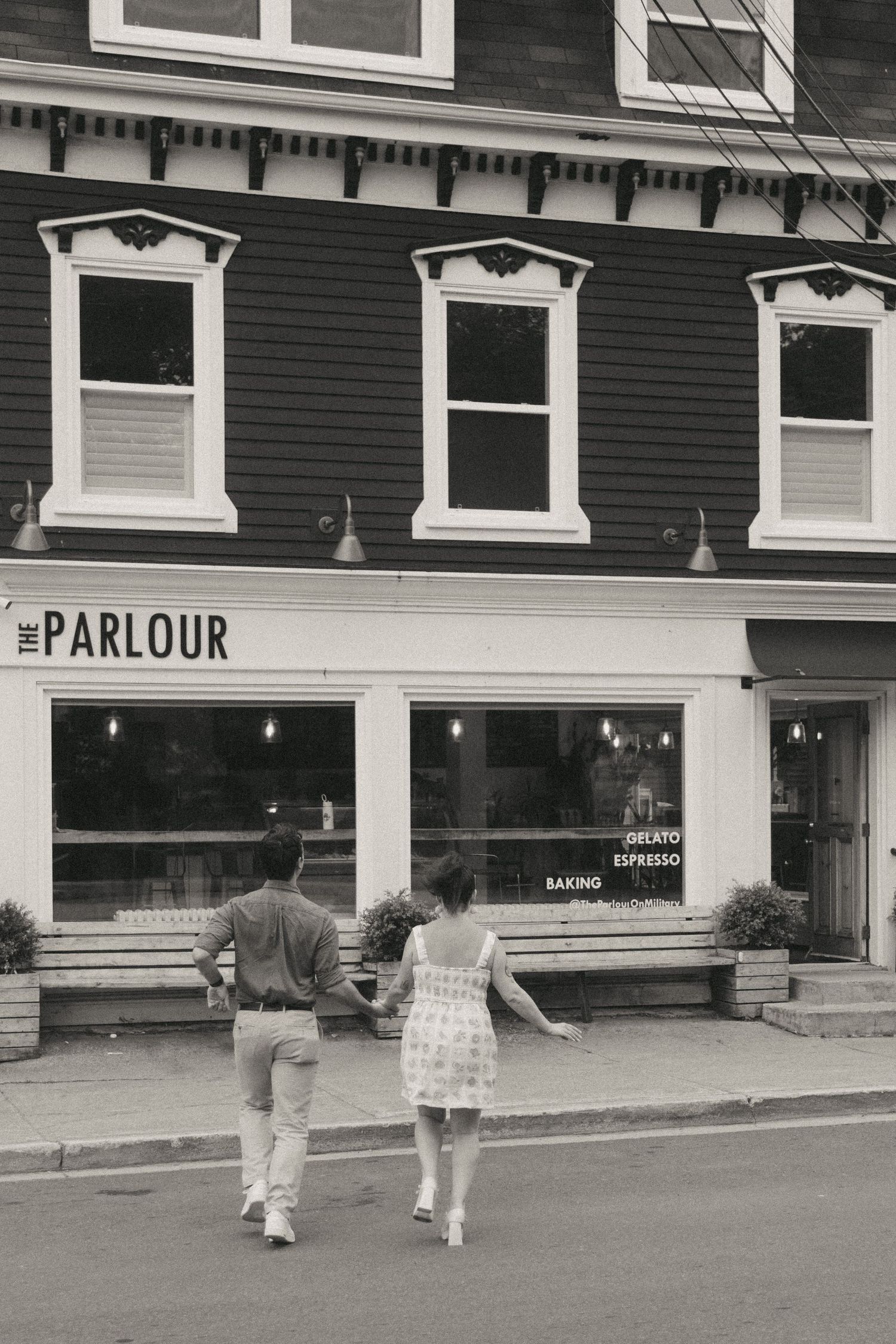 A couple walks toward The Parlour storefront with white-trimmed windows on a historic black building.