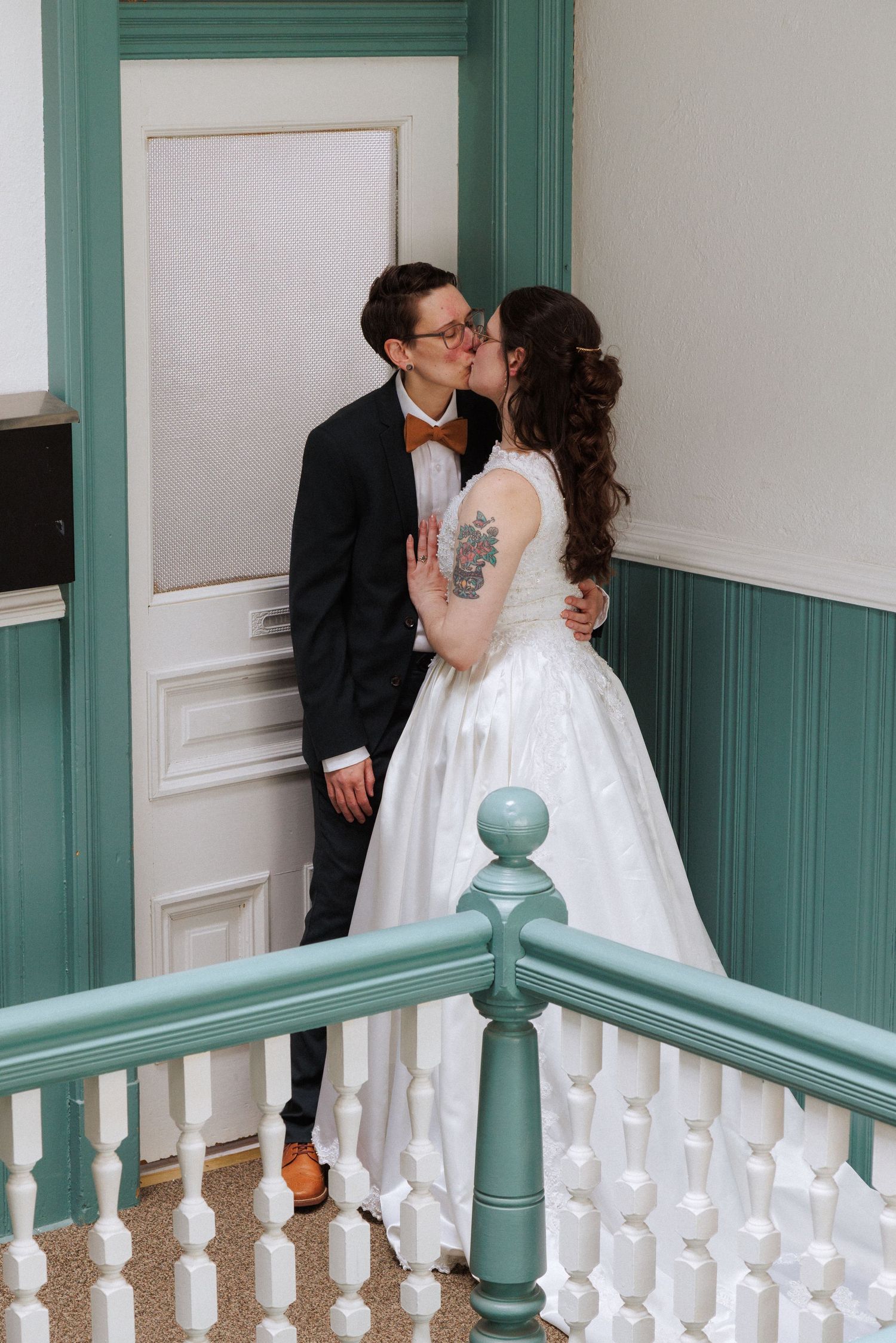 Bride and groom share an intimate moment on a staircase with white railings and sage green accents.