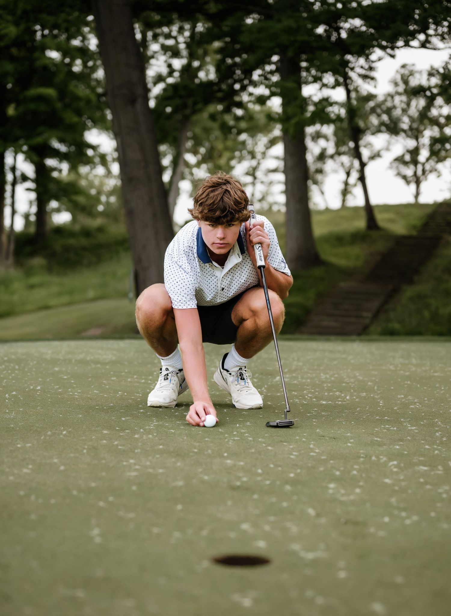 Golfer crouches low to analyze the putting green surface from multiple angles at a golf course.