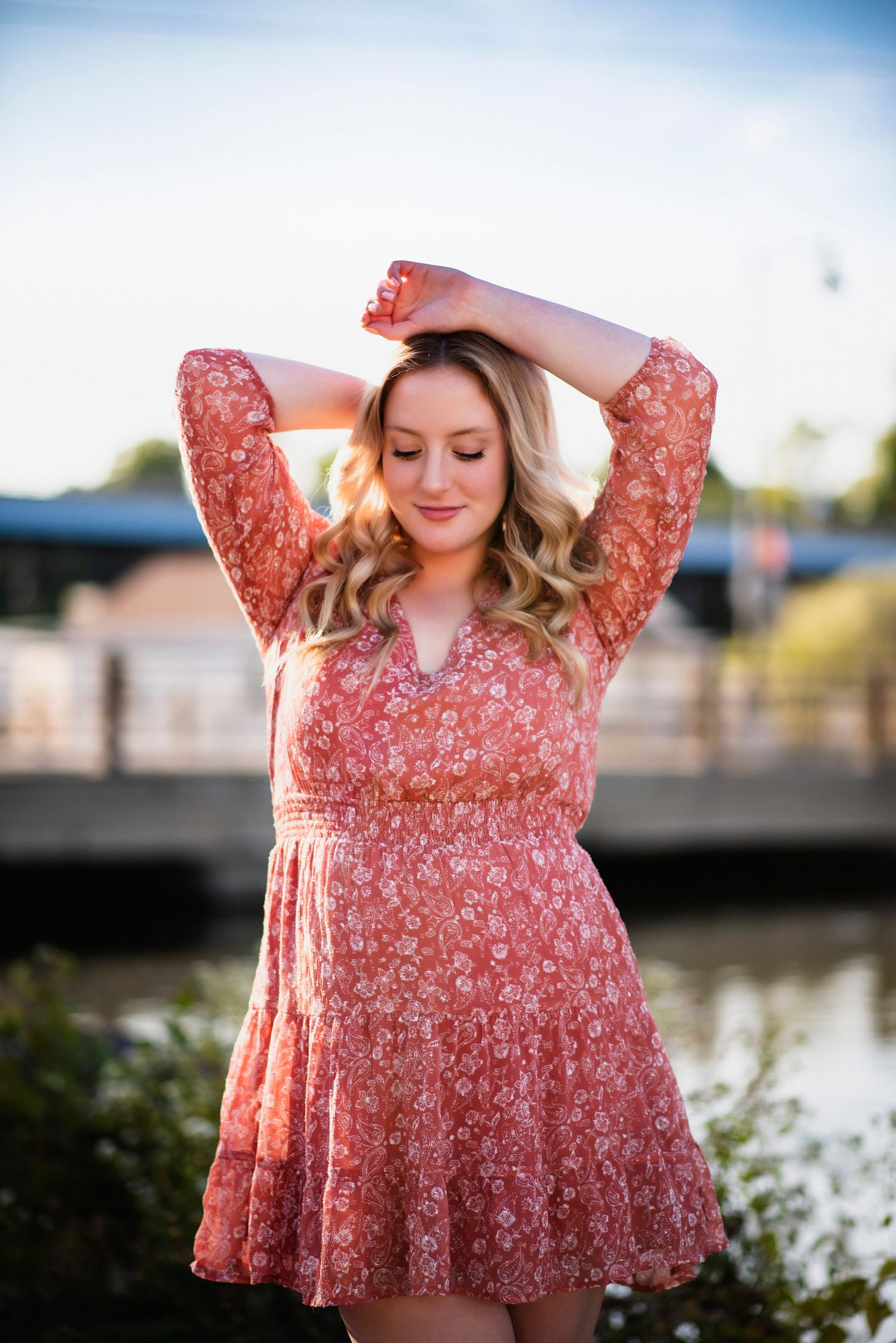 Outdoor portrait series in a coral floral dress by a waterfront during sunset.