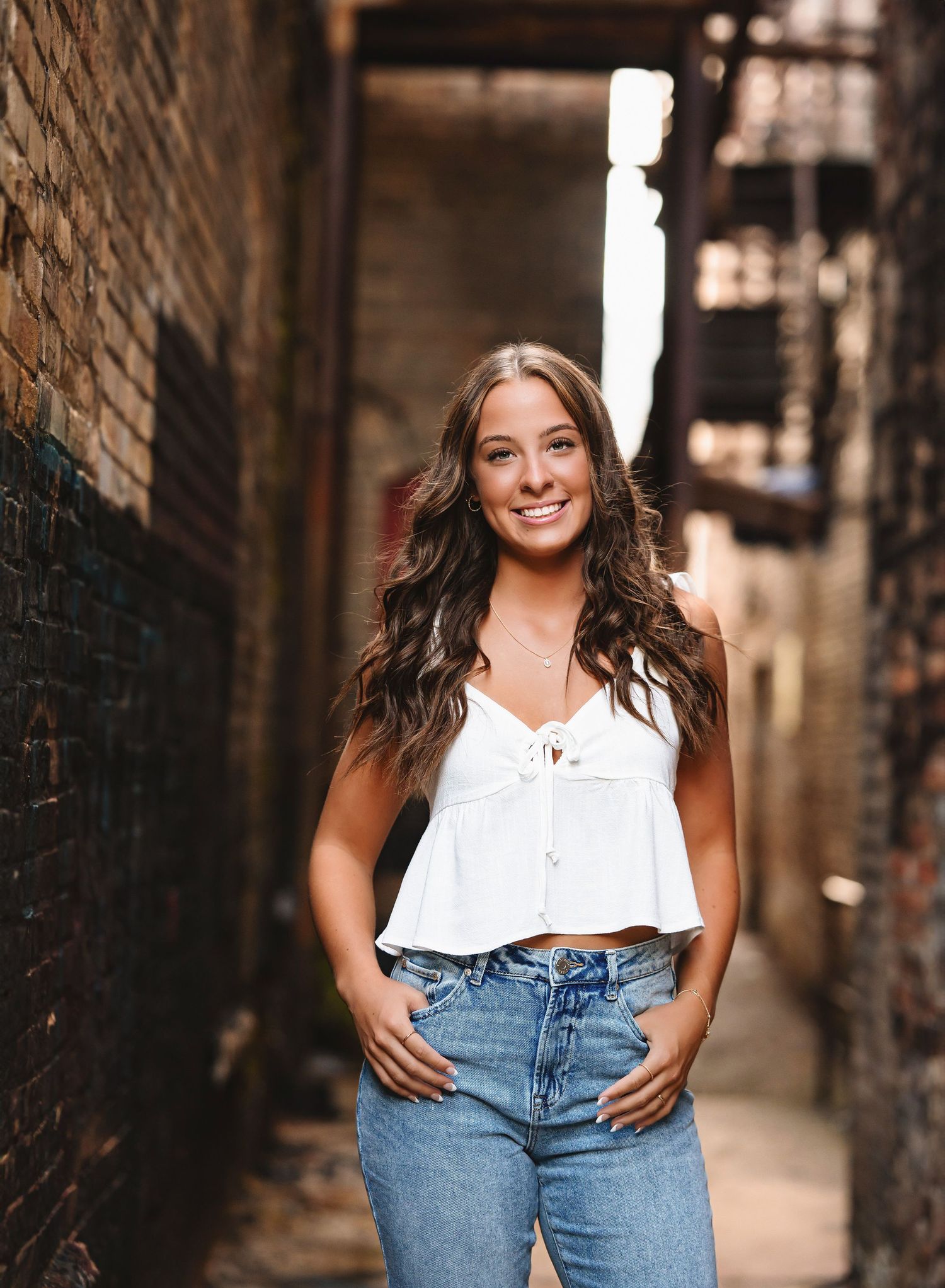 Urban senior portrait series featuring someone in a white sleeveless top and blue jeans.