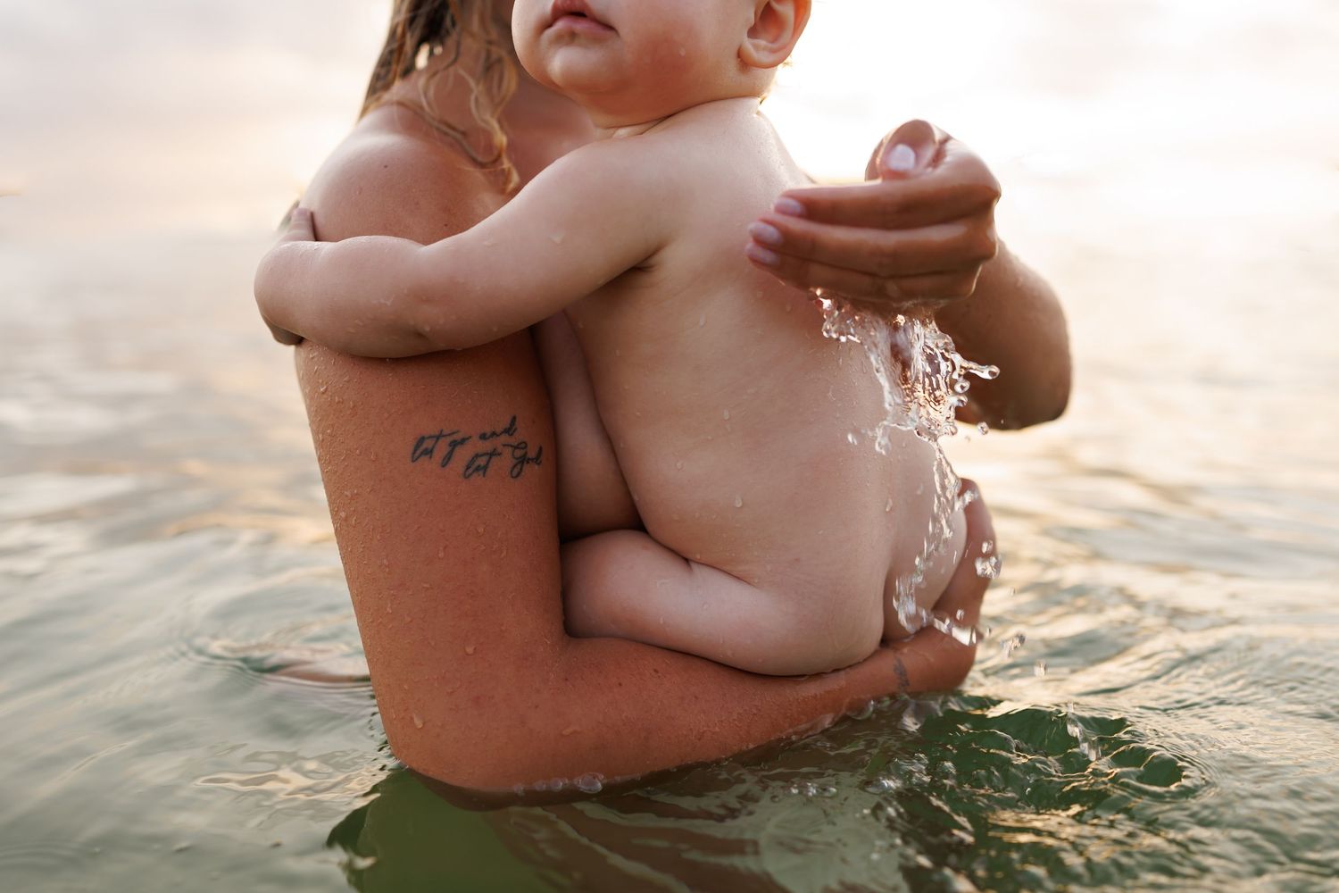 A peaceful moment in water as someone carries a small baby while swimming in golden sunlight.