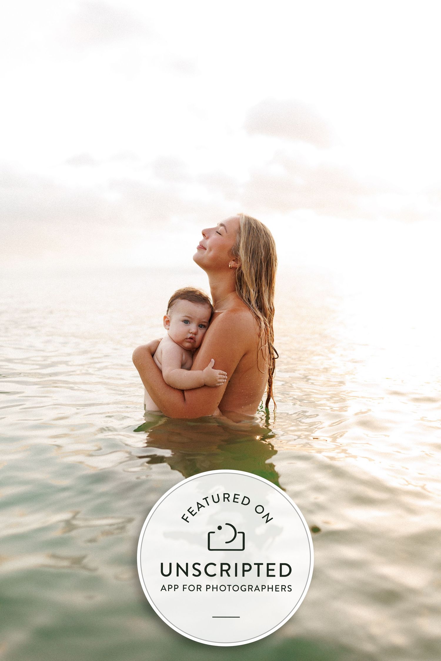 A tender moment captured in golden hour light as figures embrace while standing in calm ocean waters at sunset.