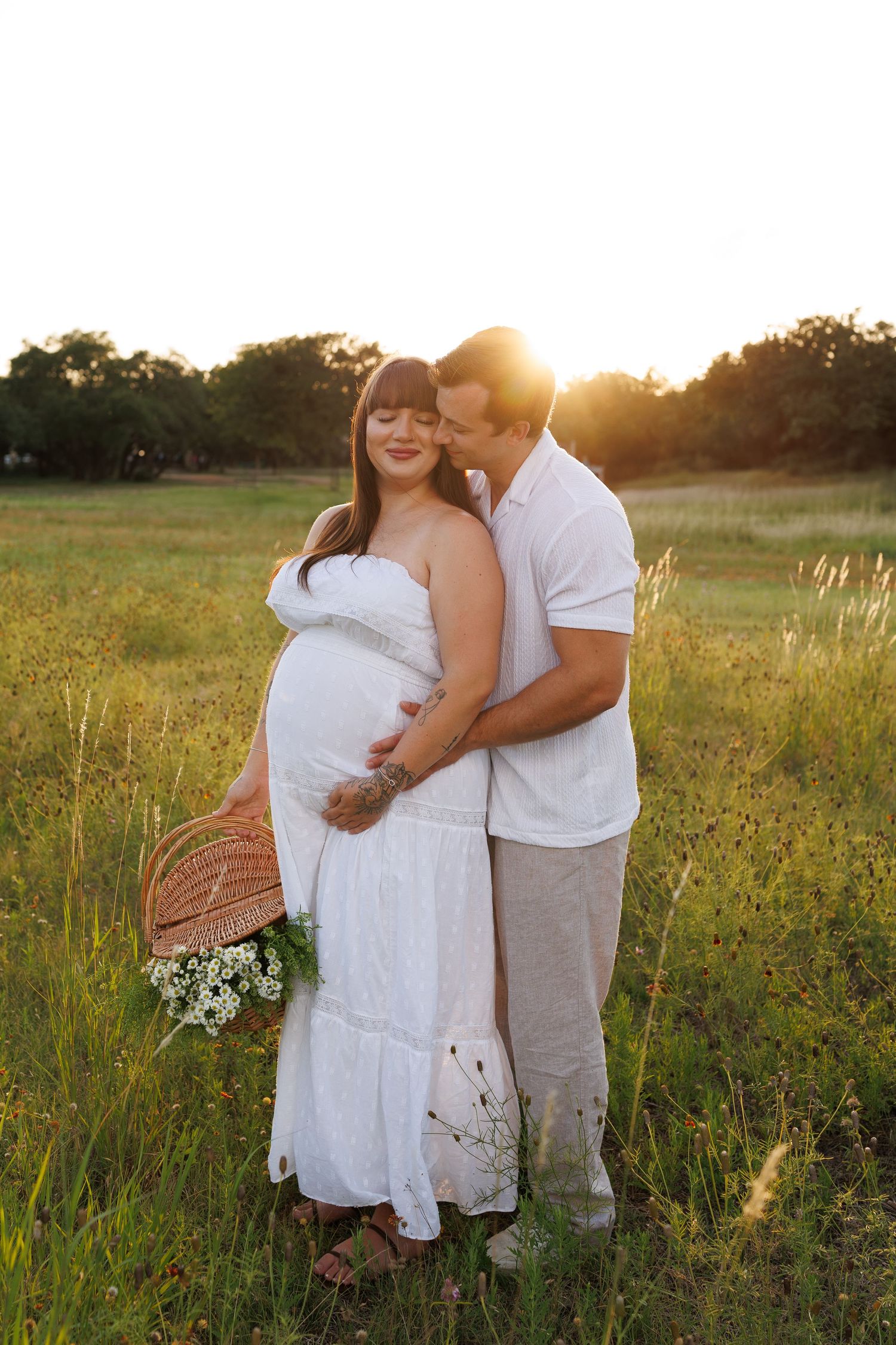 Couple embraces in golden sunlit field during sunset maternity photo shoot.