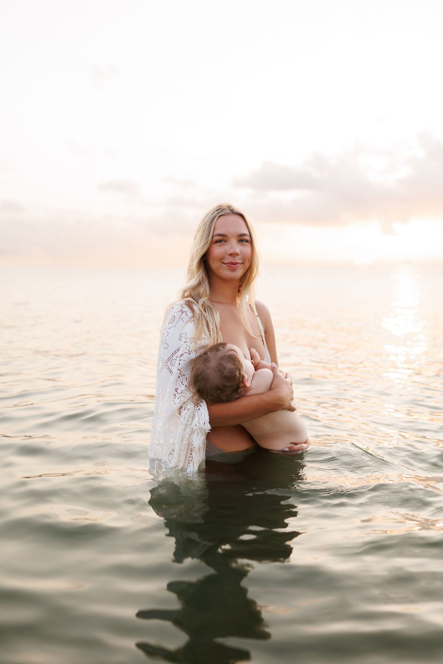 A figure stands in calming ocean waters at sunset creating a serene and ethereal atmosphere.