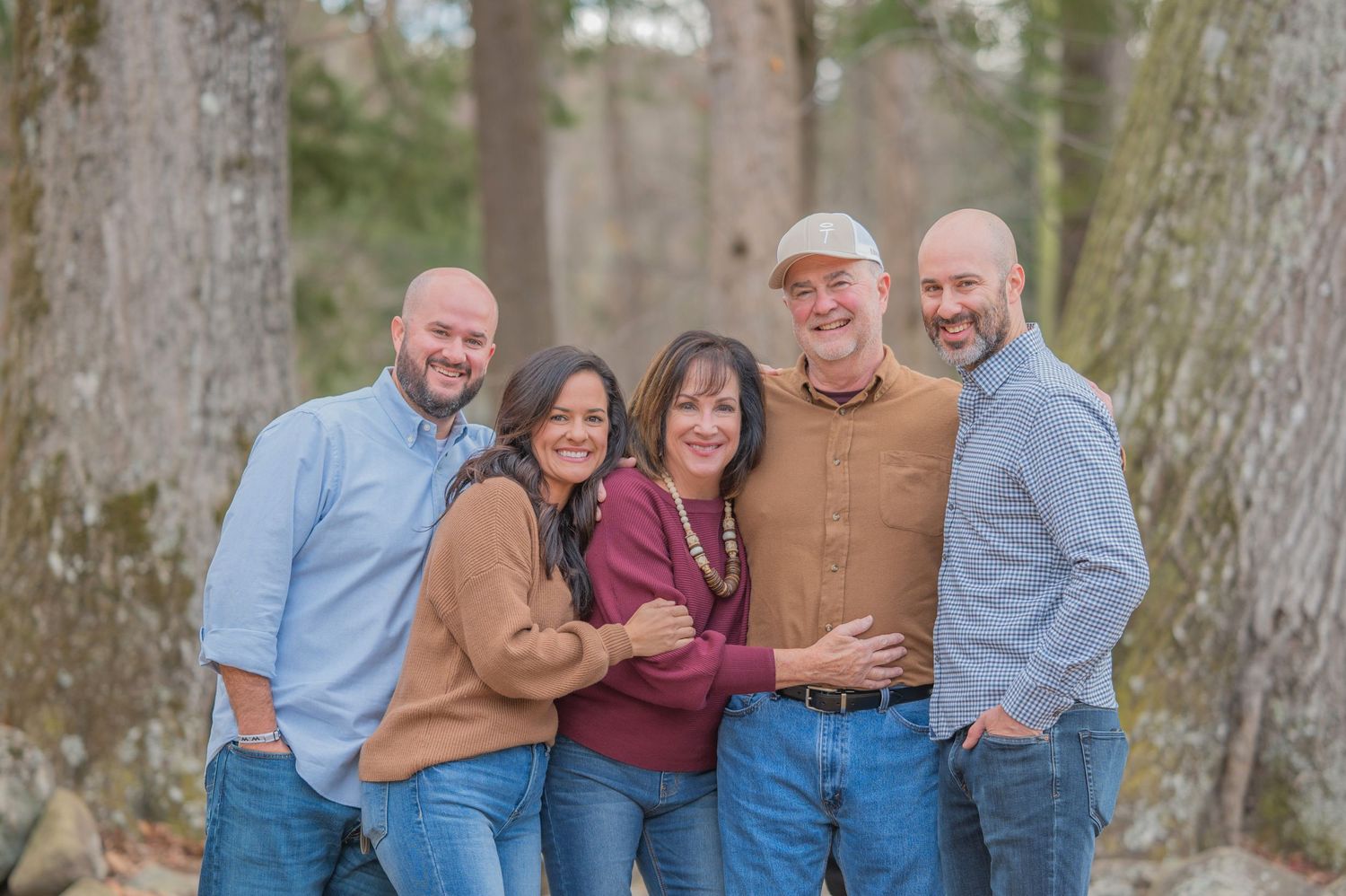 A group of people wearing casual sweaters and jeans pose together outdoors in a wooded setting by Sevierville Photographer.