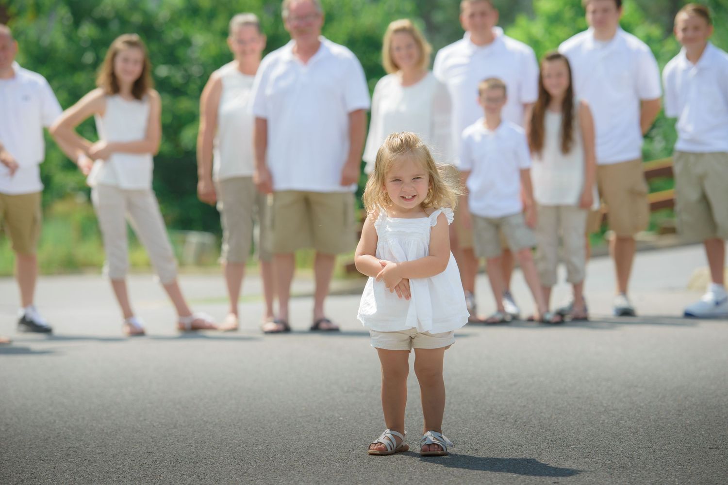 A small child in a white outfit stands on a paved path while family gather in the background in Wears Valley TN.