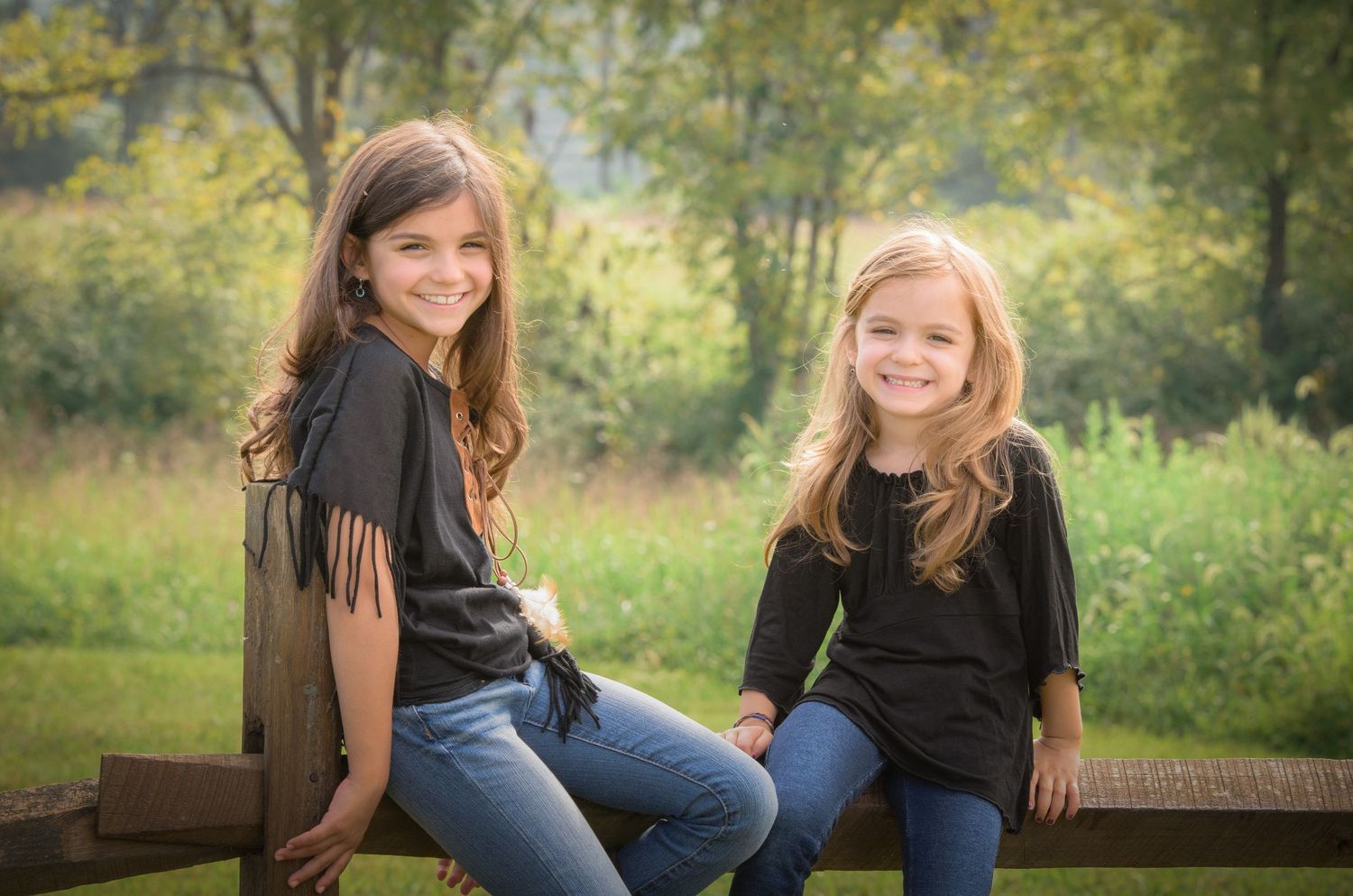 Pigeon Forge Photographer portrait of two sisters in casual clothing sit together on a wooden bench in a sunny outdoor setting.