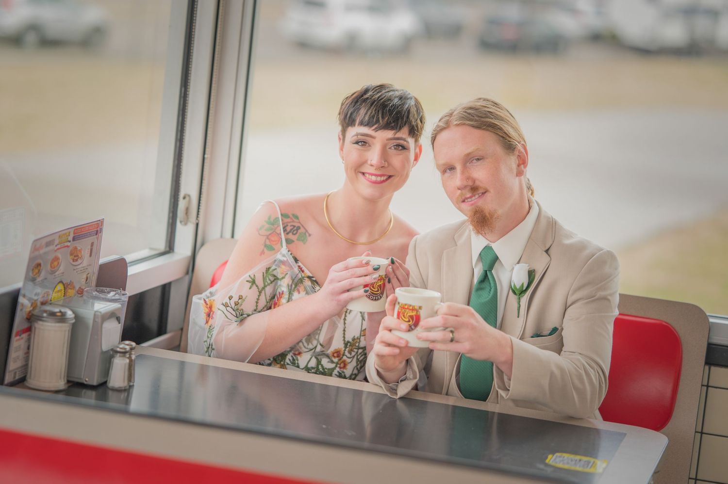 A couple in a retro style diner toasting with beverages in front of window on red booth seats by Sevierville TN Wedding Photographers.