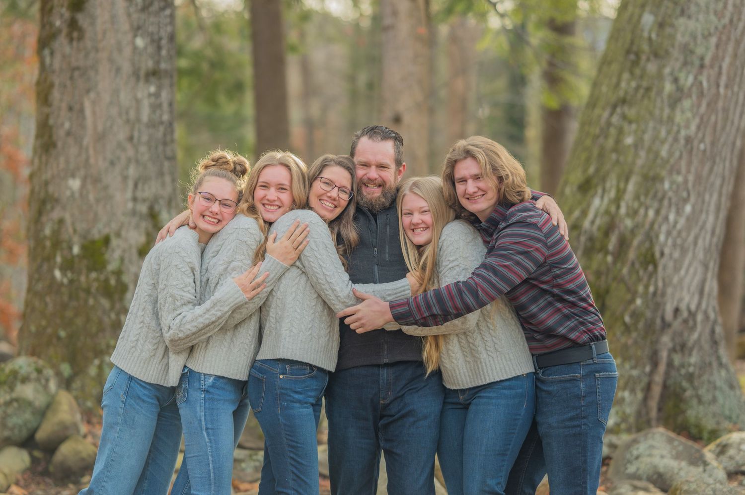 A group of people wearing cozy sweaters hugging and laughing together during an outdoor autumn photo session in the woods Cosby Tennessee.