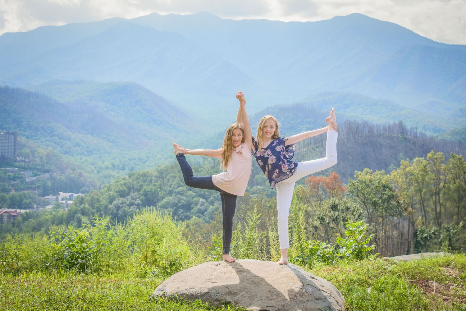 Gatlinburg photographers tn portrait of two sisters practicing yoga poses on a rock outcrop with misty mountain views.