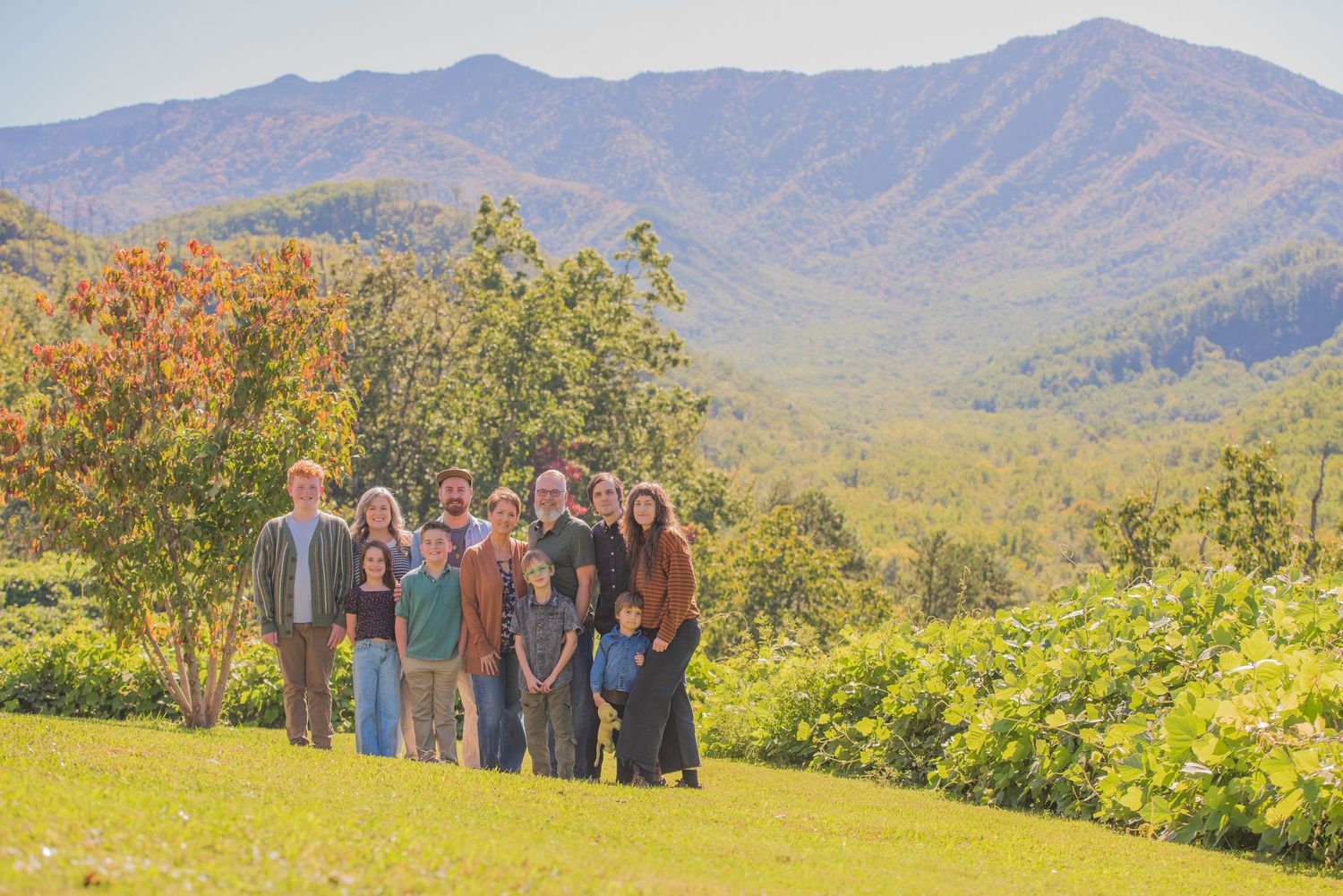 A group of people stand together on a grassy hillside overlooking the Great Smoky Mountains by Gatlinburg Photographer tn.