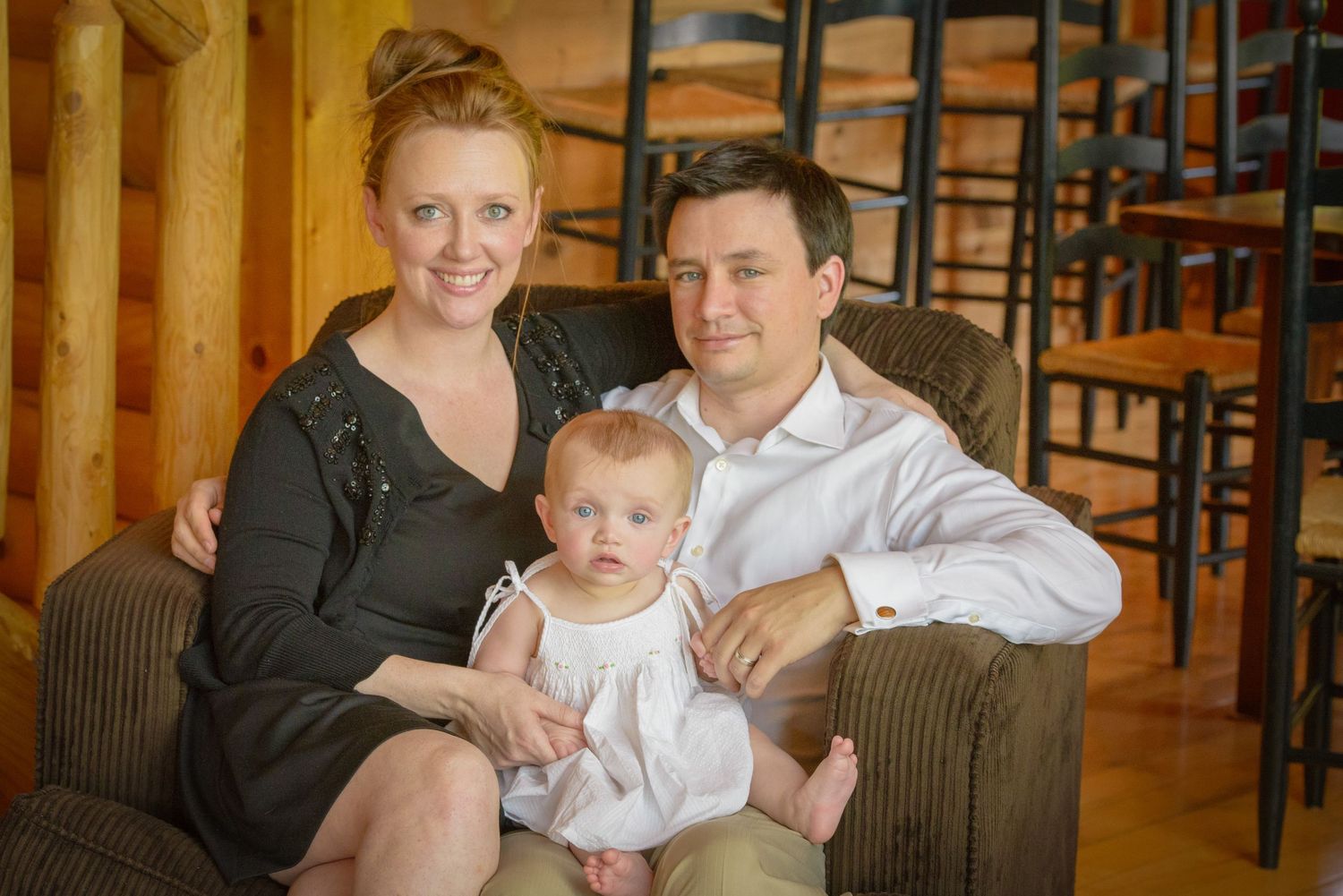 A family sits together on a brown couch in a warmly lit room with wooden walls and bar stools in the background in Pigeon Forge cabin
