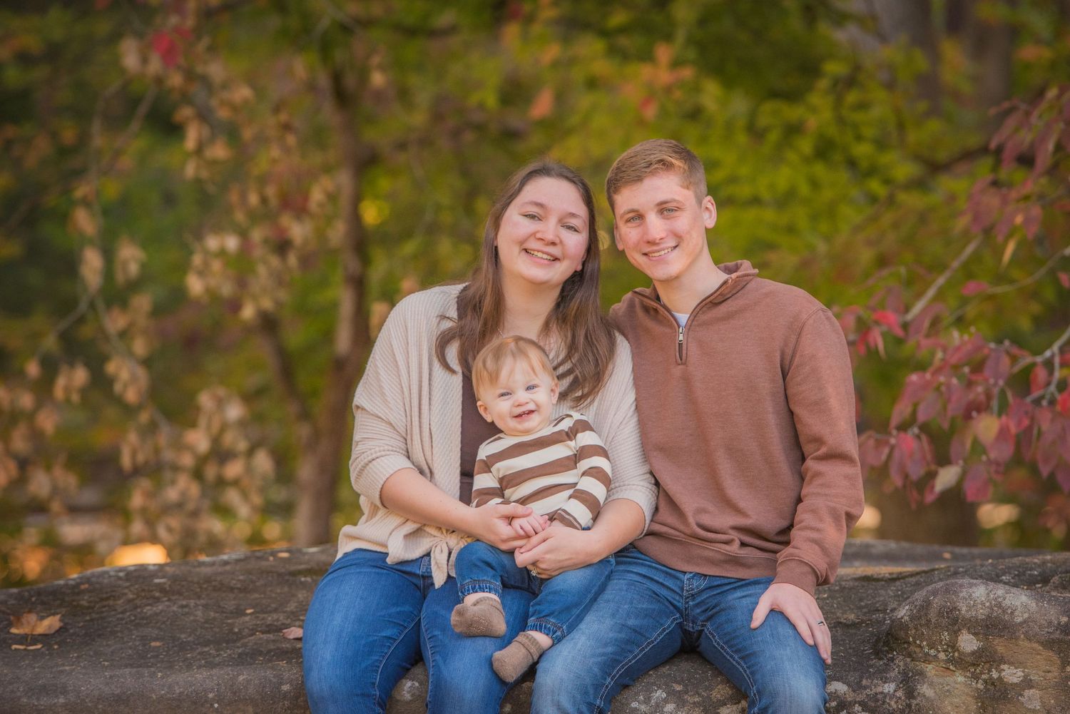 Townsend TN photographers of a family of three sitting together on a rock wall during autumn with colorful fall foliage in the background.