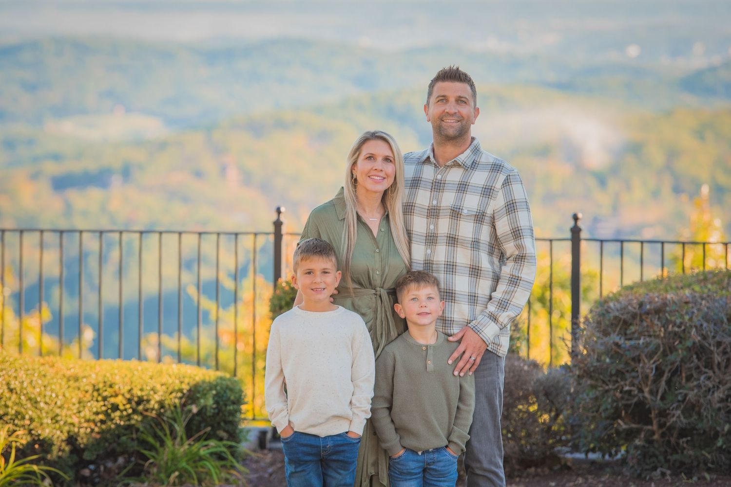 A family of four poses together outdoors against a scenic mountain landscape with yellow wildflowers in the background in Pigeon Forge TN.