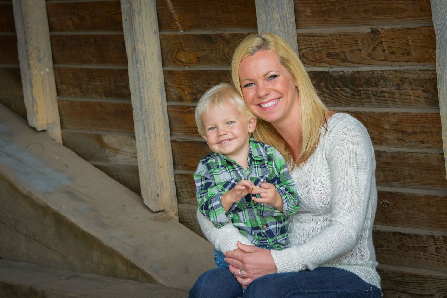 Parent and young child sit together smiling on wooden steps inside rustic bridge in Sevierville TN.