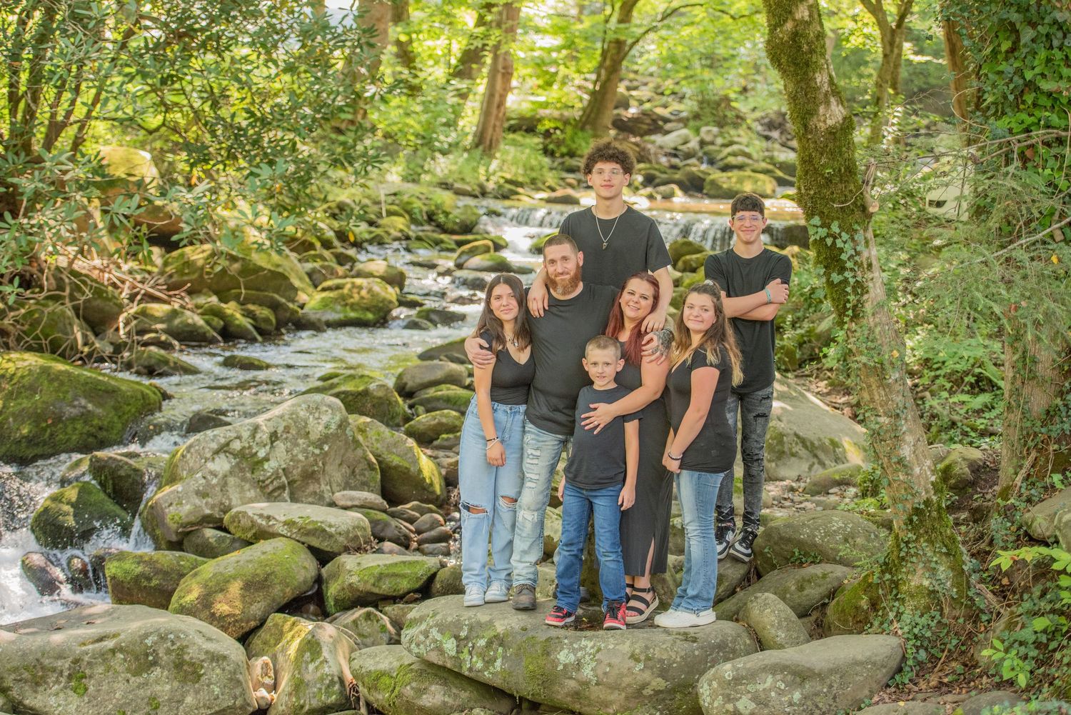 A group poses together on mossy rocks along a flowing stream in a lush forest setting in Cosby TN.