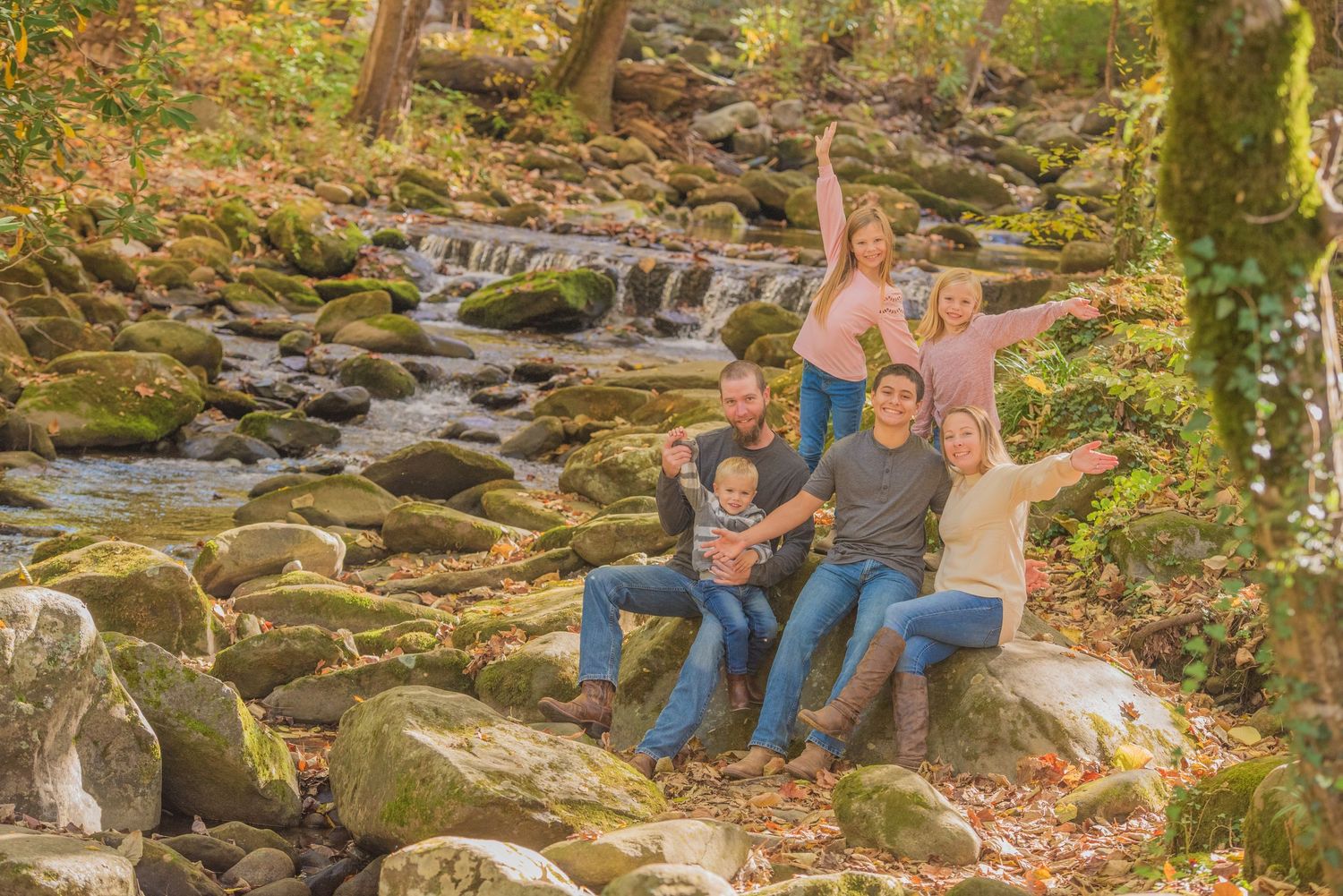 A family sits on mossy rocks by a cascading stream in an autumn forest setting by Gatlinburg photographers tn.