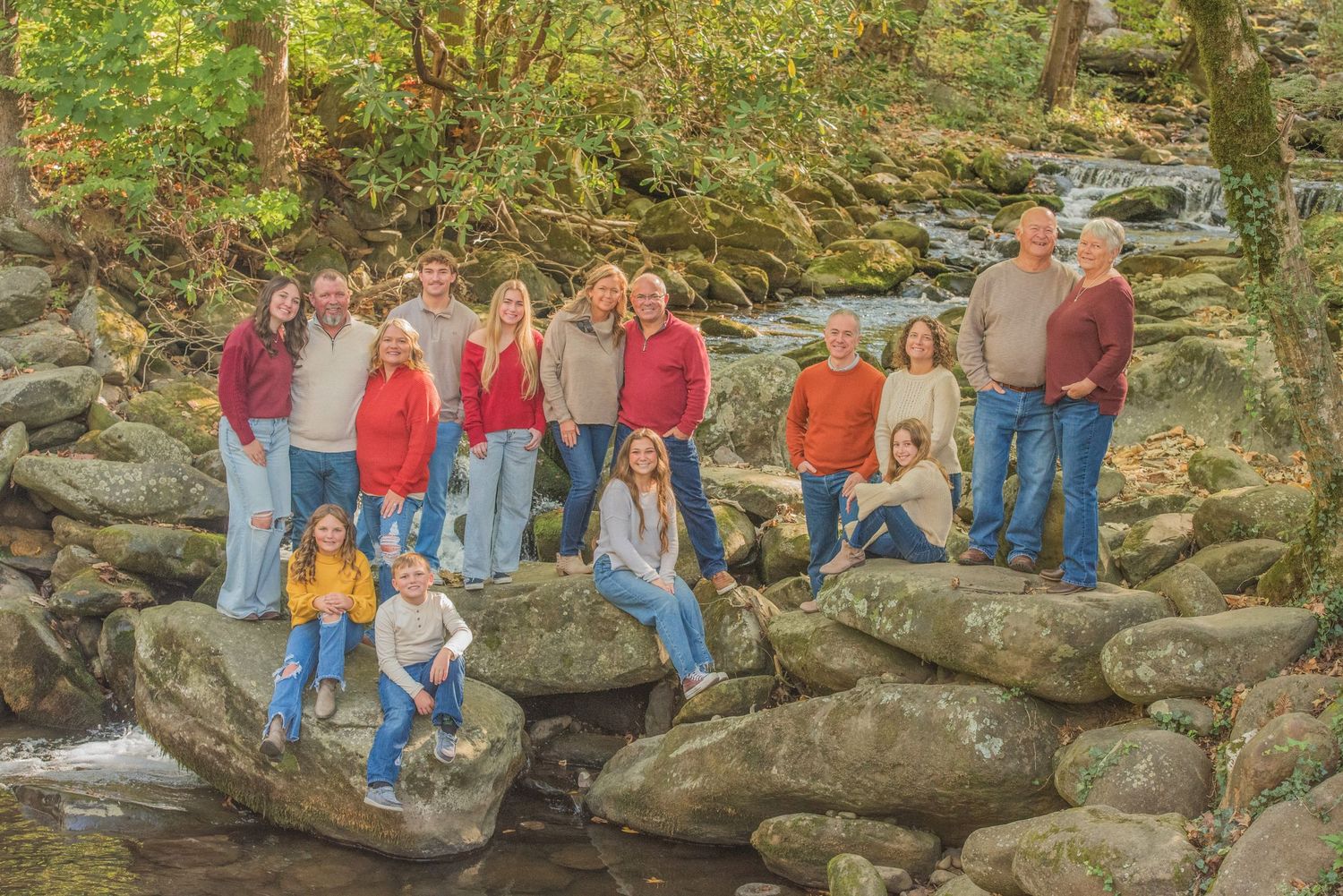 A group of people standing together on large rocks beside a flowing creek in a wooded forest setting.