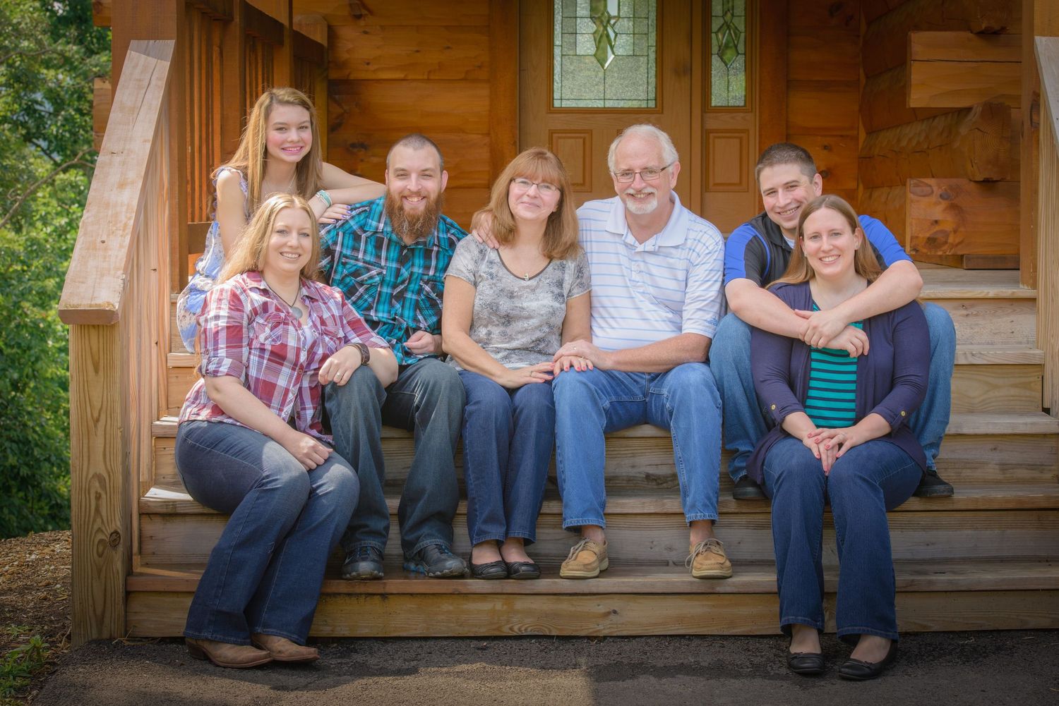 A family sits together on wooden steps of a rustic cabin porch during a sunny outdoor family photo session Sevierville TN.
