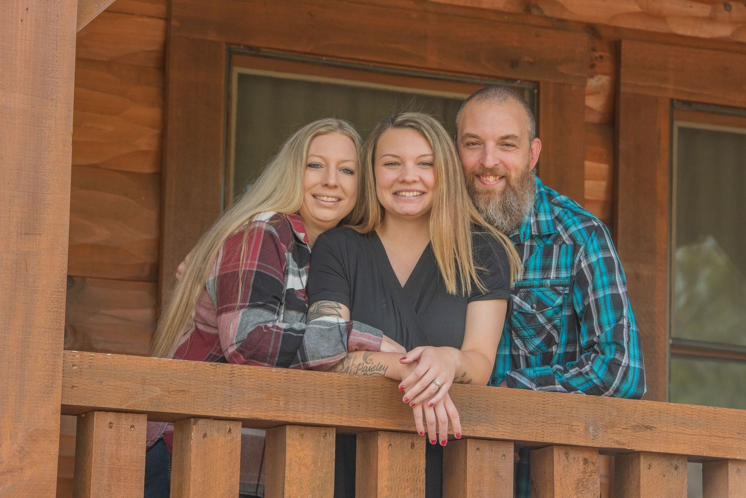 Family smile together while standing on a wooden cabin porch with rustic log siding in the background in Pigeon Forge TN.