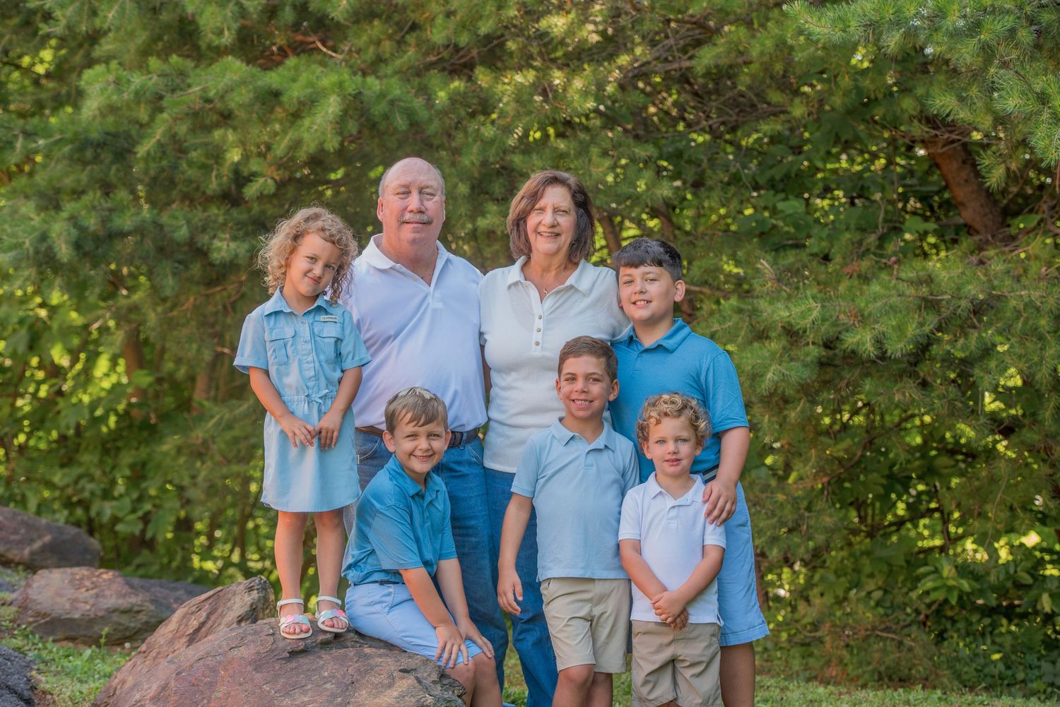 Multi-generational group in coordinating blue outfits poses outdoors against green foliage background at their cabin in Sevierville TN.