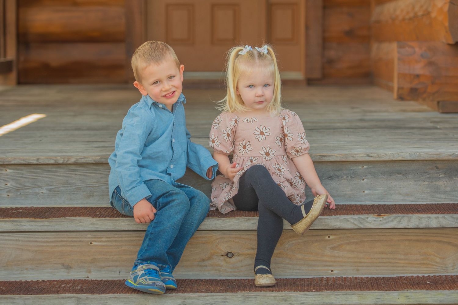 Two small children wearing casual outfits sit together on wooden steps at their cabin rental in Pigeon Forge TN.