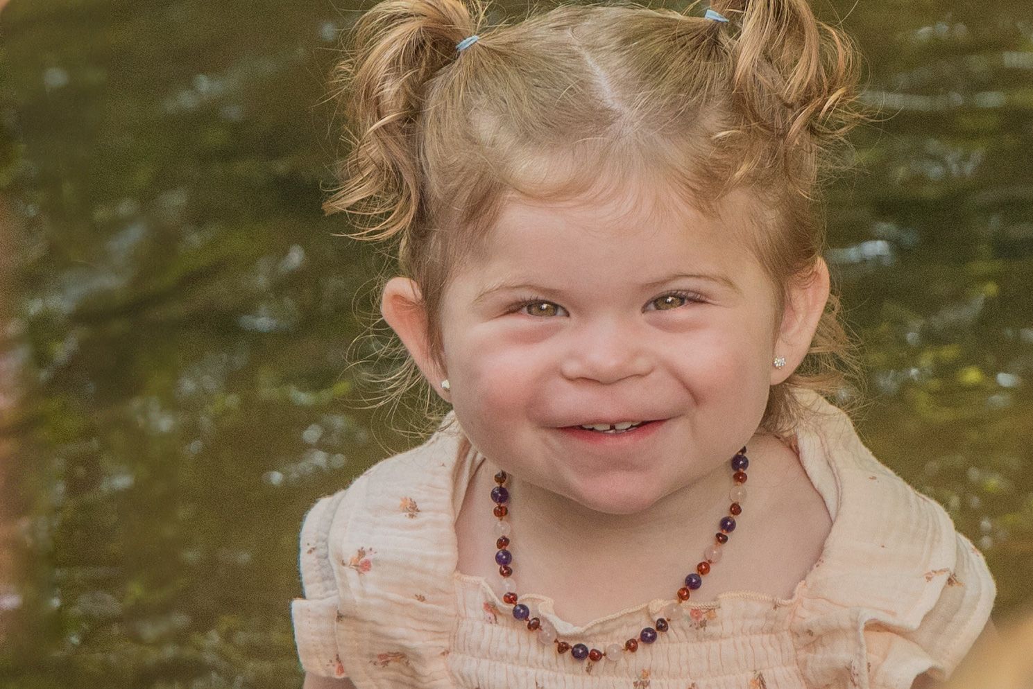 A young child smiles while wearing a cream-colored dress and colorful beaded necklace outdoors in Pigeon Forge TN.