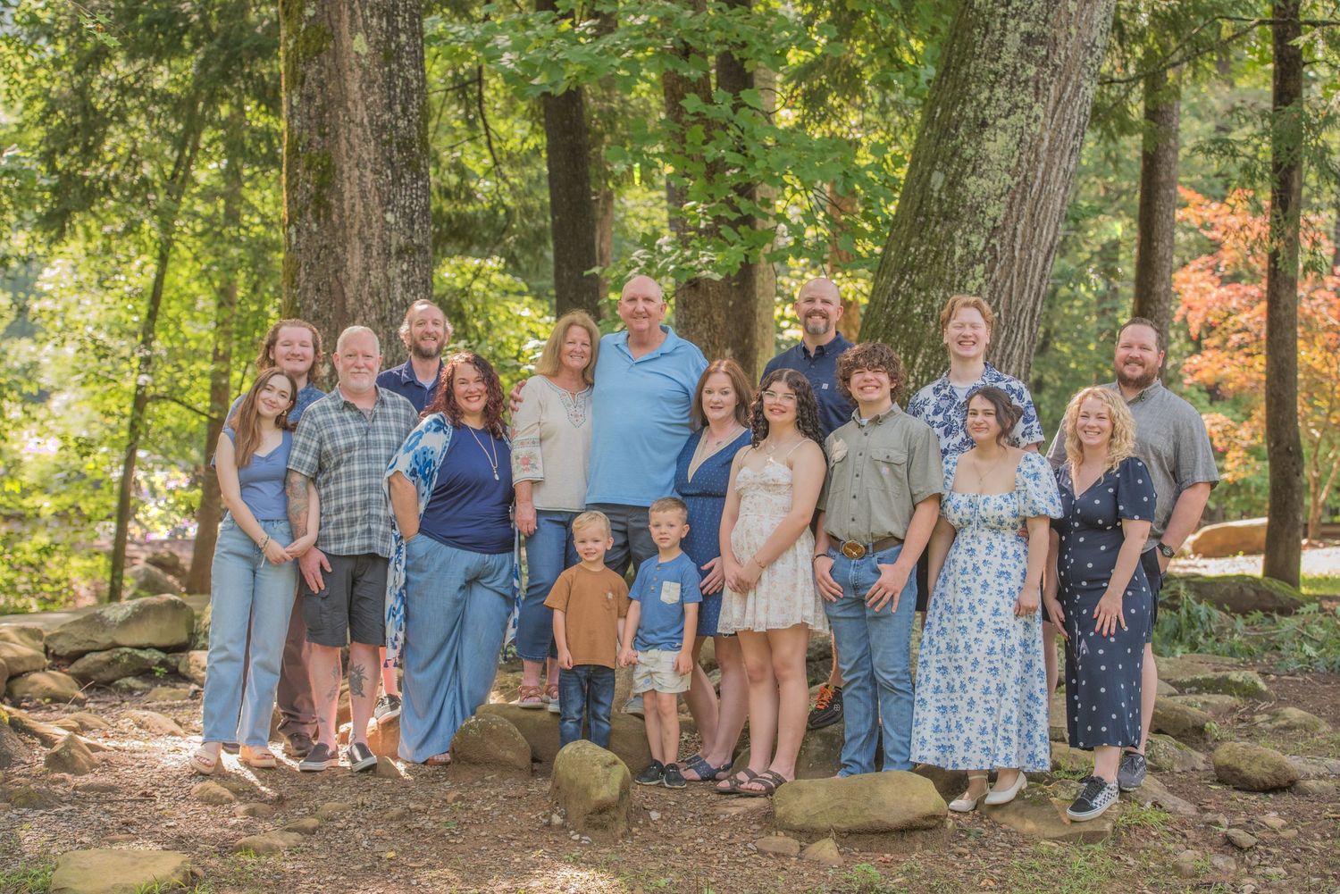 Large family reunion dressed in coordinating blue and white outfits poses together in a wooded outdoor setting during summer in Cosby TN.