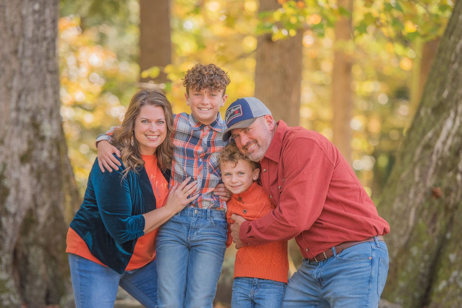 Family of four poses together outdoors during autumn with trees and golden sunlight in background by Gatlinburg TN photographer.