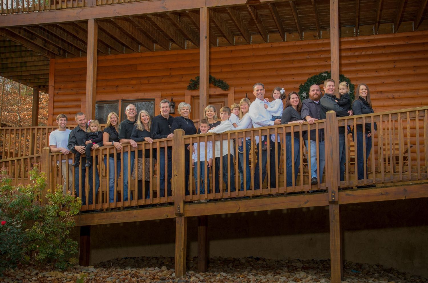 A family stands together on a wooden deck railing of a rustic log cabin building during an outdoor gathering in Pigeon Forge TN.