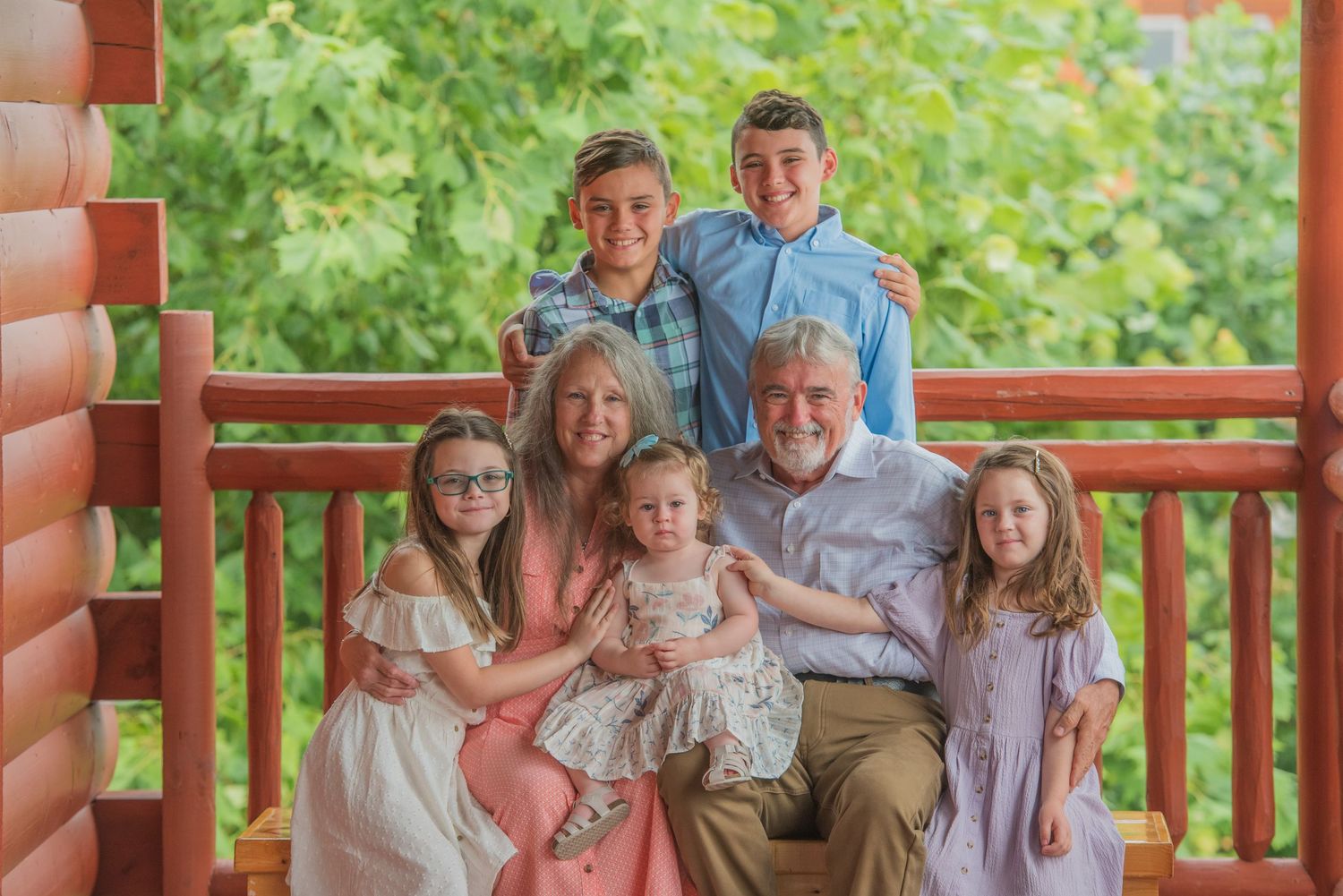 Multi-generational family portrait on rustic wooden porch with natural greenery backdrop by Pigeon Forge TN photographers.