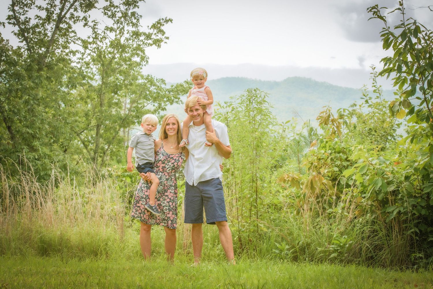 Family enjoying a summer day together on a grassy hilltop with green mountains in the background by Gatlinburg TN Photographers.