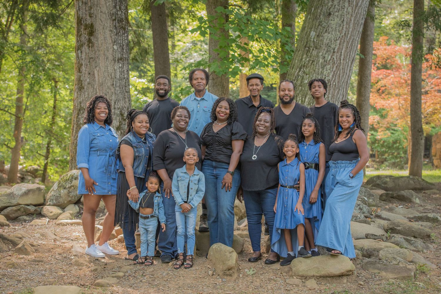 Large family group wearing coordinated blue outfits poses together outdoors in a wooded natural setting in Sevierville TN.