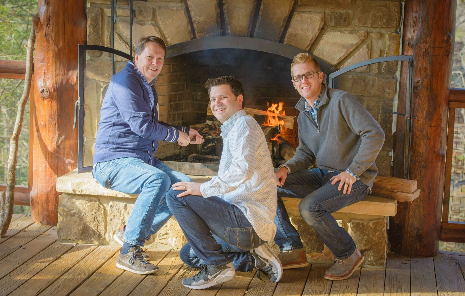 Dad and sons sit casually together on a stone ledge under a rustic wooden porch with a stone fireplace in Pigeon Forge TN.