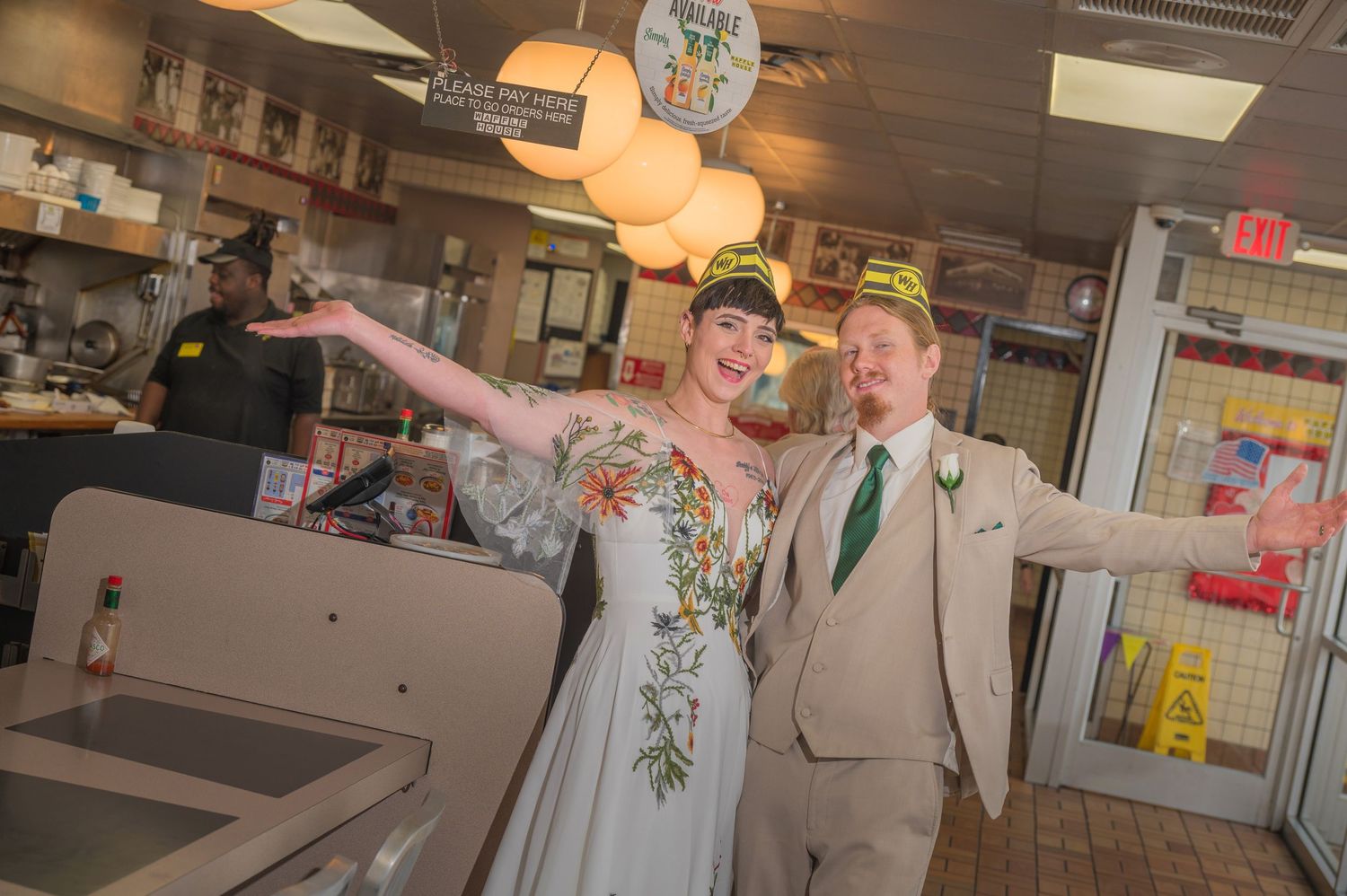 A newlywed couple strikes celebratory poses inside a casual restaurant with disco ball and pendant lighting overhead by Gatlinburg Weddings.