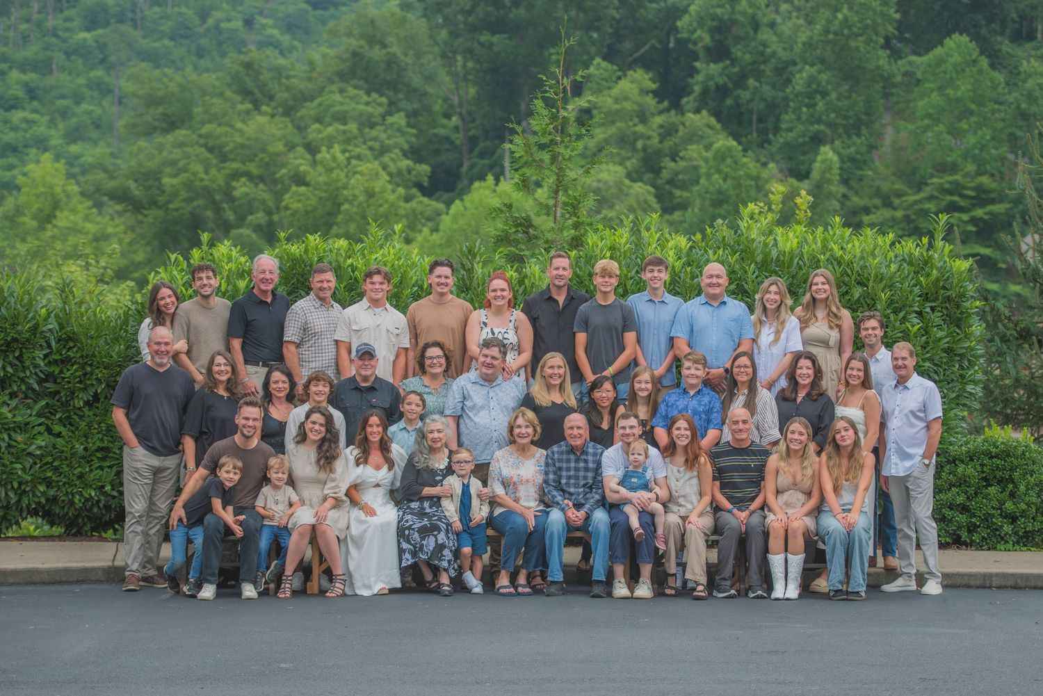 Large group photo taken outdoors with green mountain landscape and trees in background on summer day.