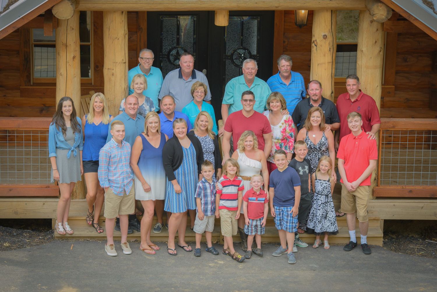 A large multi-generational family group poses together on wooden porch steps of a rustic cabin in Sevierville Tn.
